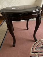 Side view of the vintage dark brown wooden side table showing the ornate carved apron and cabriole legs with curved feet on a pink rug.