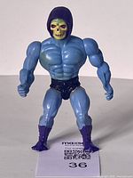 Front view of vintage Skeletor figure showing muscular blue body, green skull face with blue hood, black briefs, and purple boots.