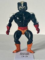 Front view of the vintage Stinkor MOTU action figure showing the black muscular body, white head stripes, red gloves and belt, orange shorts and boots.
