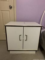 Front view of the white side night table with two closed cabinet doors and metal handles.