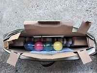 Open cardboard carrying case showing bocce balls and carrying bag inside.