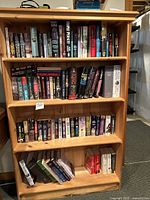 View of entire bookshelf filled with various fiction books, showing natural wood finish and four shelves.