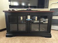 TV stand showing full front with cherry top and black bottom with two glass-paned cabinet doors.