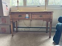 Front view of the maple finish console table with decorative brass hardware on drawers and four legs.