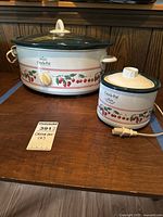 Both Crock-Pot slow cookers on wooden table, showing the cherry motif and glass/cream lids