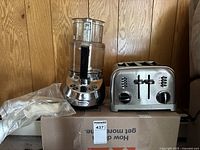 Food processor and toaster shown together on a cardboard box with a wood panel background.