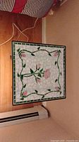 Close-up of the ceramic tiled tabletop showing pink roses and green leaves in mosaic pattern with a green tile border.