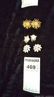 Photo showing three pairs of clip-on flower earrings arranged vertically on a dark fabric background with MaxSold lot tag labeled 469.