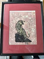 Front view of the framed Chinese print on canvas featuring a yellow and black tiger standing on a rock with abstract background, in a dark frame with red matting.