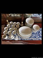 Photo showing cups, creamer, sugar bowl, and stacks of various bowl and plate types on a blue floral tablecloth.