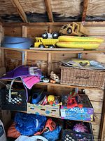Shelf with yellow inflatable pool floats, toy trucks, large wicker basket, and assorted toys below including Aqua Barbells game box