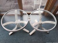 Two round tables with clear textured glass tops and white metal frames.