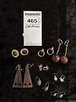 Top view of all earrings spread on black fabric with auction tag visible.