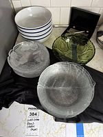 Full view of the entire lot showing white ceramic bowls, frosted glass plates, green Arcoroc bowls, and clear salad bowls with nutcracker bowl and tool