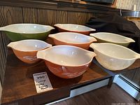 Seven vintage Pyrex mixing bowls arranged on a table showing various colors and sizes in the Autumn Harvest pattern