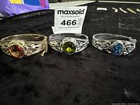 Three vintage style metal bracelets with colored stones on a black surface, showing front and top views.