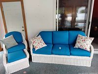 Full view of white wicker sofa and matching armchair with ottoman, blue cushions, and throw pillows