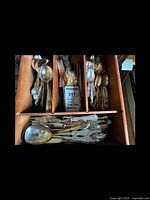 Top view of utensil set arranged in wooden drawer organizer showing forks, spoons, knives with visible floral pattern and engraving.