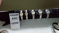Photo showing six women's wrist watches in silver and gold metal bands on a black velvet display roll.