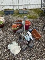 Photo shows two tall metal crane sculptures, two owl figures, small rectangular planters, round terracotta and glazed pots, and two cast lily pad garden ornaments.