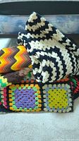 Multiple hand knit afghan blankets folded and stacked showing different patterns and colors