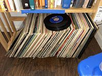 Large selection of vintage vinyl albums and 45s stored upright under a bookshelf with some additional books above them.