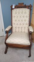 Front view of antique Eastlake style rocking chair showing tufted cream upholstery and carved wood design.