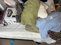 Photo showing the assorted blankets stacked on a bed with the boxed Eddie Bauer WiFi Smart Electric Throw in plaid visible behind them.