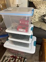 Stack of three clear plastic storage bins with string lights boxes inside, showing blue and white handles