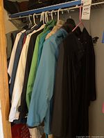 Multiple women's jackets and rain coats hanging on a rod, including light blue, green, white, and black items.
