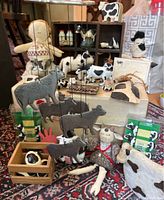 Multiple cow-themed items including fabric doll, metal mobile, figurines, soap dispenser, and novelty kitchen items arranged on a surface.
