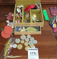 Top view photo showing coins, jewelry box with various small pins, cufflinks and jewelry pieces including the feather brooch and decorative pins