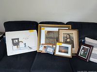 Group of framed prints including Mona Lisa and some smaller framed photos on a sofa, with one large unframed print rolled off to the side (excluded from sale)
