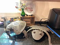 Metal frog and turtle figurines on counter with wooden crate in background, green bottle with button flowers, and decorative white plate with red text.