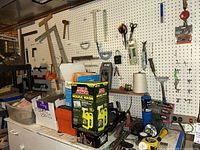 Full view of pegboard with various hand tools, scissors, string, Mold Armor house wash product, and other hardware items on a table and hanging from hooks.
