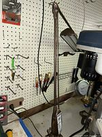 Full view of vintage Dazor industrial desk lamp with adjustable arm and clamp base, set on pegboard wall background.