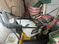 Overall view of Toro lawn mower with red engine cover and grass catcher beside yard tools and outdoor furniture.