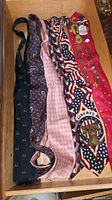 Seven men's neckties laid out on a wooden surface, showing patterns including holiday and patriotic designs.