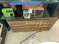 Wide view showing green portable radio, vintage clock radio, wooden printer's drawer shadow box on floor, and other small items