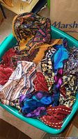 Photo of a bin filled with various ladies scarves showing different colors and patterns including red, blue, white, and black tones.