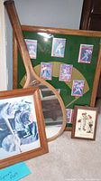 Angled photo showing four items: framed baseball cards display, vintage baseball player photo, Champion racket mirror, and Norman Rockwell print on carpet.