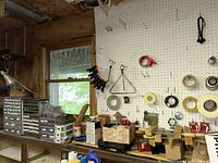 Workshop pegboard wall with multiple rolls of tape, clamps hanging, and miscellaneous small tools on workbench