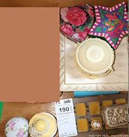 Overview of multiple trinket boxes including black heart-shaped floral box, star-shaped colorful box, ivory small container boxes. Also visible a ceramic dish with floral decoration and a display card.