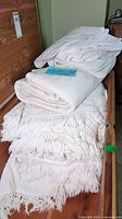 Stack of three vintage white bedspreads on wooden surface, showing various textures and fringes.