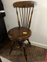 Front view of the vintage wooden swivel chair showing round seat, spindle backrest, and turned legs on casters.
