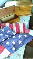 Photo showing two vintage American flags with 13 and 49 stars draped over a floral surface next to two wooden boxes, one open showing interior and Lane branding on the inside lid, the other closed with latch.