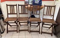 Four brown wooden folding chairs with slatted seats and backrests, arranged side by side on a tiled floor.