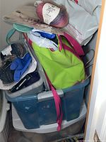 Photo showing top view of blue plastic storage bin filled with various knitting and craft supplies including a skein of 'You & Your Yarn Chloe' yarn, green tote bag, and gloves.