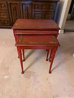 Three red nesting tables stacked inside each other showing the tops with gold detailing and legs