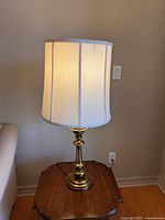Brass Stiffel table lamp standing on wooden side table next to beige sofa, illuminated, with white fabric shade.